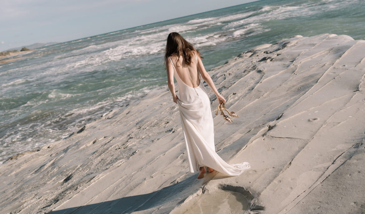 femme marchant vers la mer en robe blanche sandales à talon à la main